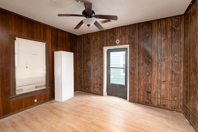 empty room with wooden walls, ceiling fan, and light hardwood / wood-style floors