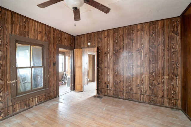 unfurnished room with ceiling fan, wood walls, and light wood-type flooring