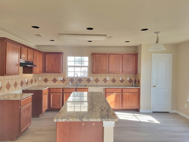 kitchen featuring light stone counters, sink, a center island, light hardwood / wood-style floors, and hanging light fixtures