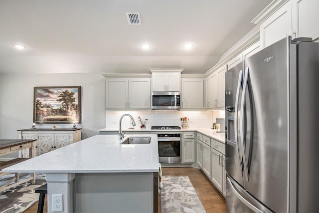 kitchen with stainless steel appliances, sink, backsplash, a kitchen island with sink, and light stone counters