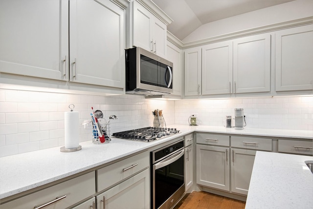 kitchen featuring light stone counters, vaulted ceiling, stainless steel appliances, and tasteful backsplash