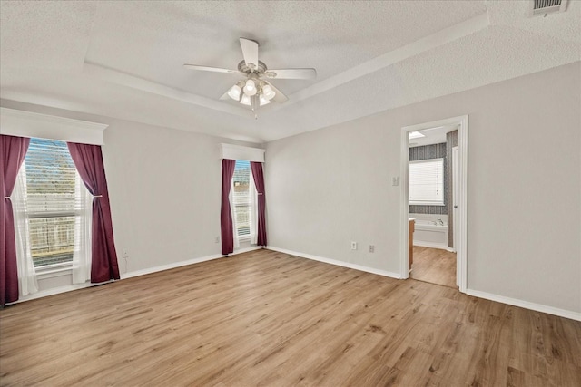 spare room with a tray ceiling, ceiling fan, a textured ceiling, and light wood-type flooring