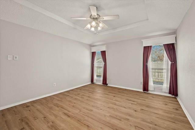 unfurnished room featuring plenty of natural light, a raised ceiling, a textured ceiling, and light hardwood / wood-style flooring