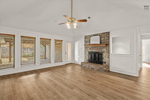 unfurnished living room with ceiling fan, a brick fireplace, light hardwood / wood-style floors, vaulted ceiling, and a textured ceiling