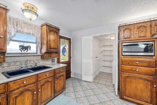 kitchen with stainless steel microwave, sink, decorative backsplash, and a textured ceiling