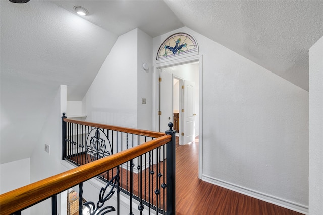 corridor featuring hardwood / wood-style flooring, lofted ceiling, and a textured ceiling