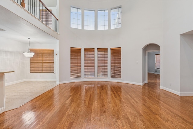 unfurnished living room with an inviting chandelier, a high ceiling, and light hardwood / wood-style flooring