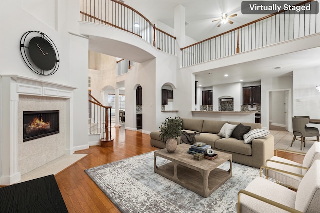 living room with a tile fireplace, a towering ceiling, ceiling fan, and light hardwood / wood-style flooring