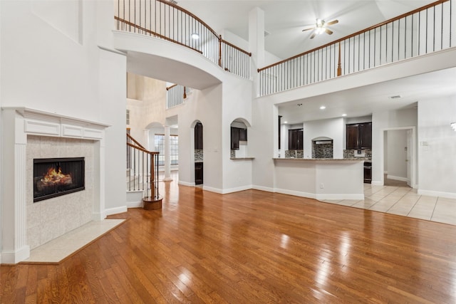 unfurnished living room with ceiling fan, light hardwood / wood-style floors, a tile fireplace, and a towering ceiling