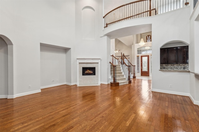 unfurnished living room featuring a tiled fireplace, hardwood / wood-style floors, and a high ceiling