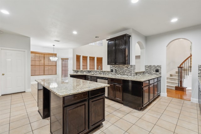 kitchen featuring backsplash, kitchen peninsula, hanging light fixtures, light tile patterned floors, and dark brown cabinetry