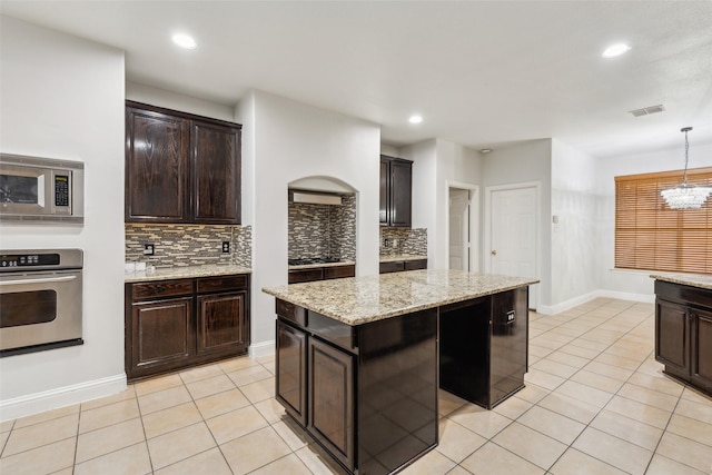 kitchen with appliances with stainless steel finishes, decorative light fixtures, a kitchen island, and dark brown cabinets