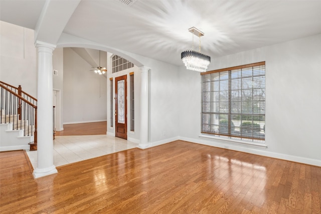 spare room with ceiling fan with notable chandelier, light hardwood / wood-style flooring, and ornate columns