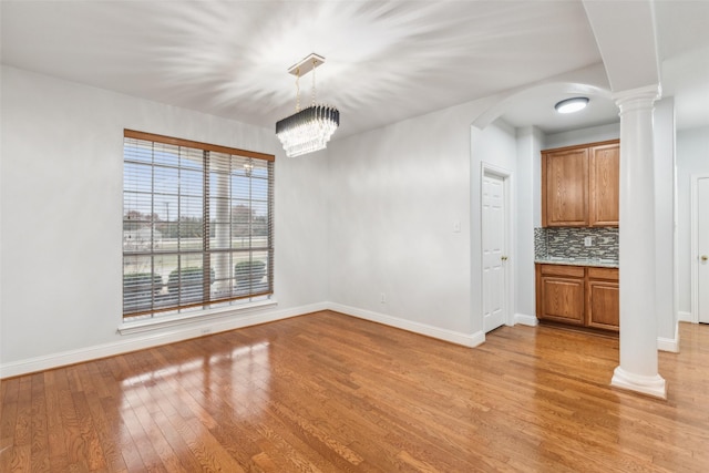 unfurnished dining area featuring a notable chandelier, light wood-type flooring, and ornate columns