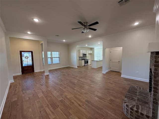 unfurnished living room with sink, crown molding, a brick fireplace, hardwood / wood-style flooring, and ceiling fan