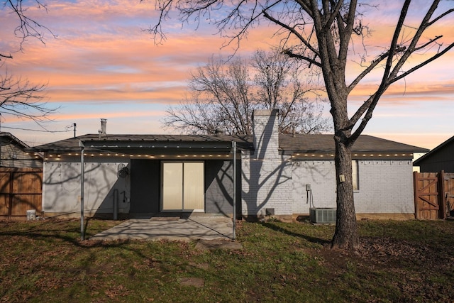 back house at dusk featuring a yard, a patio area, and central AC