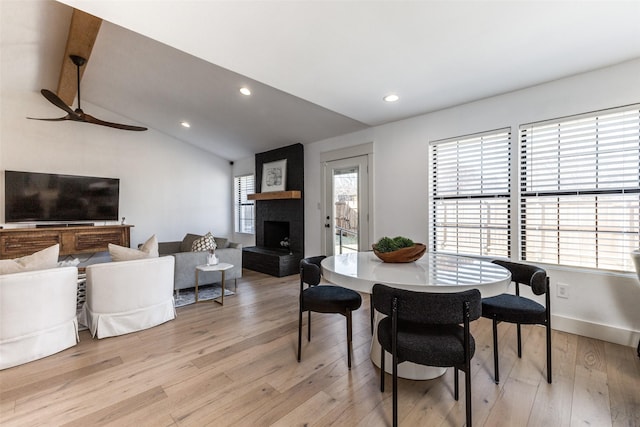 dining room featuring light wood-type flooring, vaulted ceiling with beams, and a brick fireplace