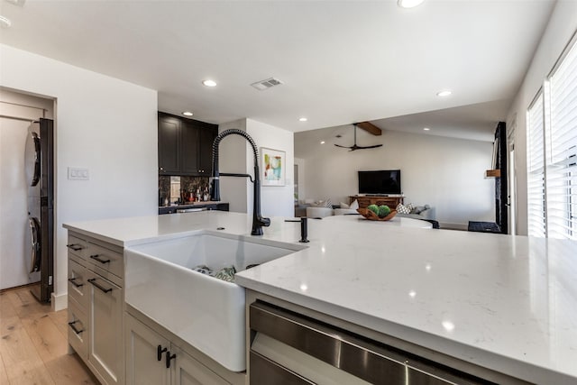 kitchen featuring light stone countertops, decorative backsplash, black fridge, sink, and light hardwood / wood-style floors