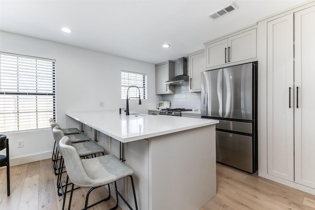 kitchen featuring stainless steel refrigerator, sink, wall chimney exhaust hood, a kitchen breakfast bar, and light wood-type flooring