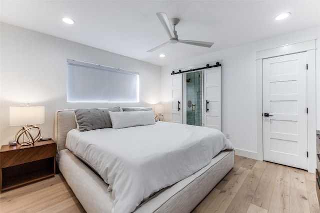 bedroom with a barn door, light hardwood / wood-style floors, ceiling fan, and connected bathroom