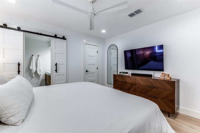 bedroom featuring ceiling fan, a barn door, and light hardwood / wood-style floors