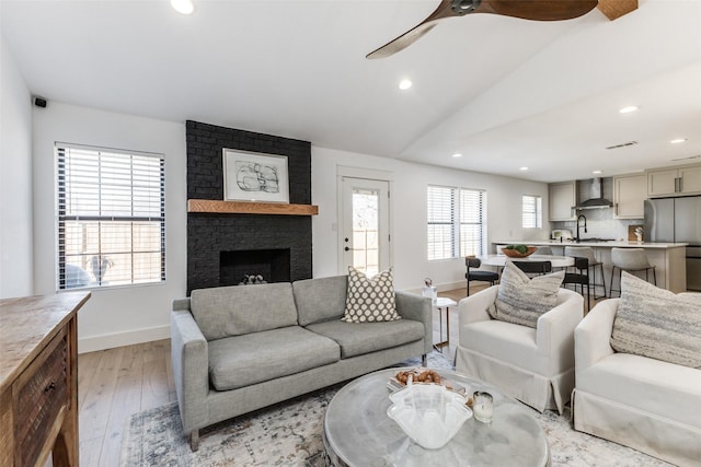 living room featuring sink, light hardwood / wood-style floors, vaulted ceiling, and a brick fireplace