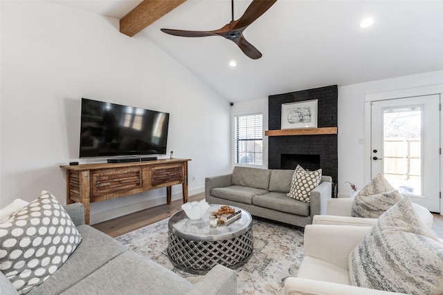 living room with a brick fireplace, lofted ceiling with beams, light hardwood / wood-style flooring, and ceiling fan