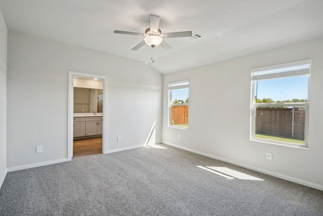 unfurnished bedroom with carpet, connected bathroom, multiple windows, and ceiling fan