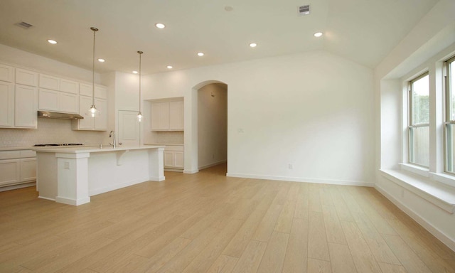 kitchen featuring tasteful backsplash, an island with sink, pendant lighting, lofted ceiling, and light wood-type flooring