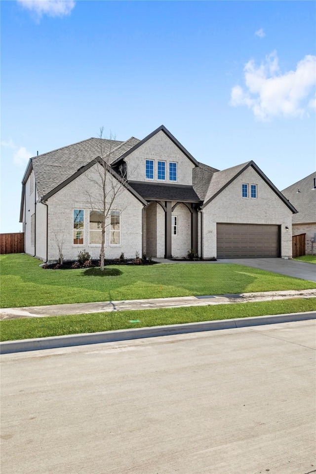 french country style house featuring a garage, driveway, a front lawn, and roof with shingles