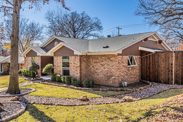 view of front of house featuring a yard, brick siding, roof with shingles, and fence