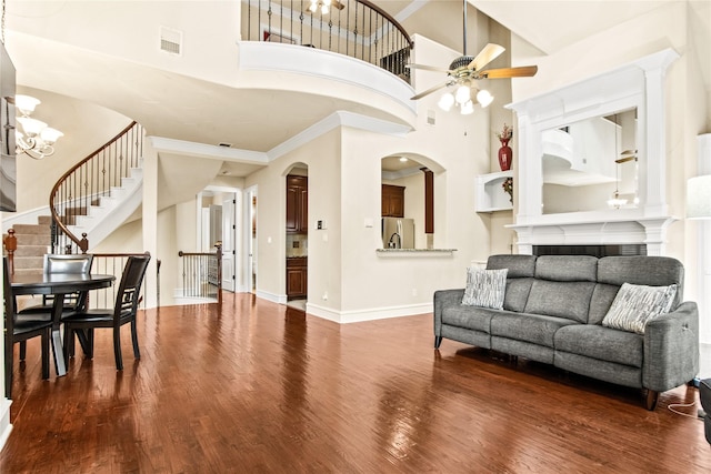 living room with a towering ceiling, ornamental molding, ceiling fan with notable chandelier, hardwood / wood-style flooring, and a fireplace