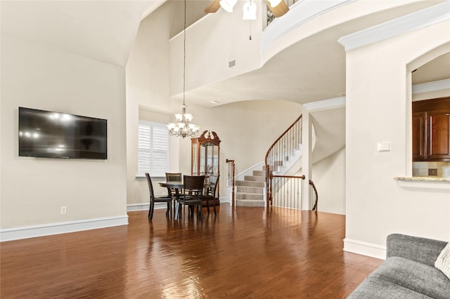 dining room with hardwood / wood-style flooring, a towering ceiling, ceiling fan with notable chandelier, and ornamental molding