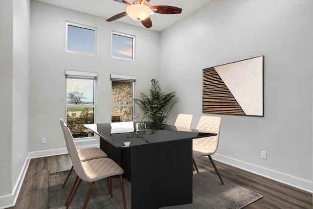 dining room with dark wood-type flooring, a towering ceiling, a ceiling fan, and baseboards