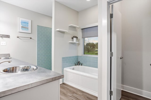 bathroom featuring double vanity, a garden tub, a sink, and wood finished floors