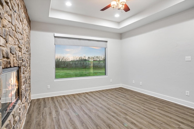 empty room featuring a ceiling fan, baseboards, wood finished floors, and a stone fireplace