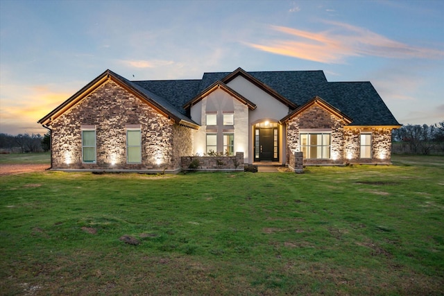 view of front facade featuring stone siding, a shingled roof, a front yard, and stucco siding