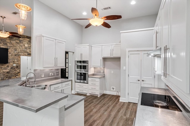 kitchen featuring stainless steel double oven, under cabinet range hood, a peninsula, a sink, and visible vents