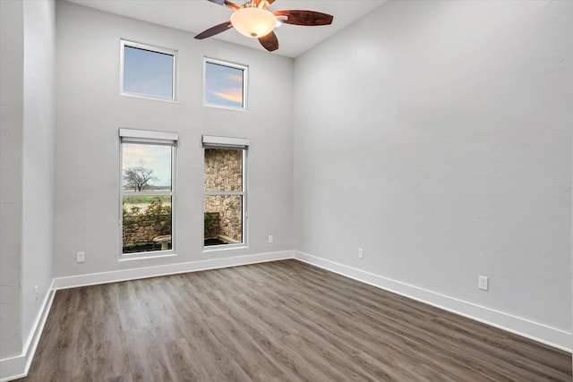 empty room with dark wood-style floors, a high ceiling, baseboards, and a ceiling fan