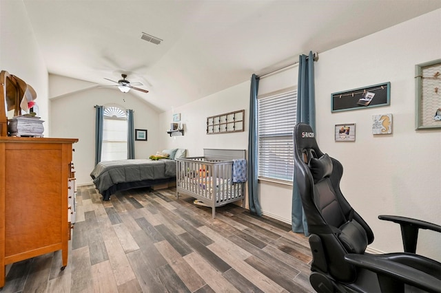 bedroom with dark hardwood / wood-style flooring, vaulted ceiling, a nursery area, and ceiling fan