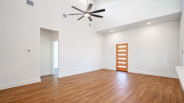 spare room with a towering ceiling, light hardwood / wood-style floors, and ceiling fan