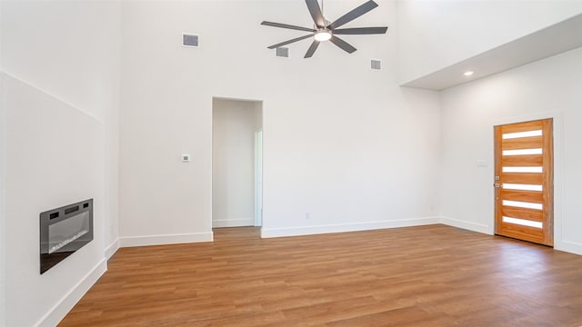 unfurnished living room featuring a high ceiling, heating unit, light hardwood / wood-style floors, and ceiling fan