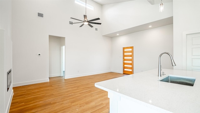 kitchen with ceiling fan, sink, light stone countertops, light hardwood / wood-style flooring, and a towering ceiling