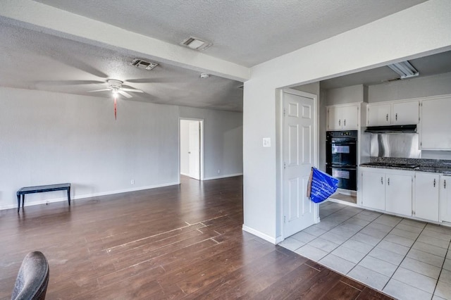 kitchen with white cabinets, light wood-type flooring, a textured ceiling, and double oven