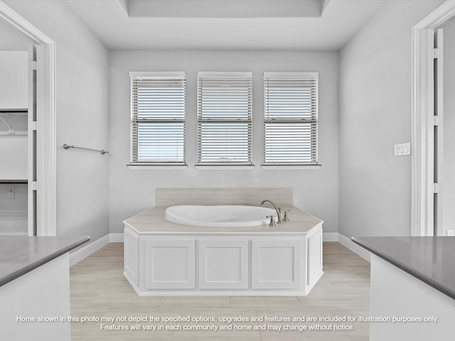bathroom with baseboards, a walk in closet, a garden tub, and vanity