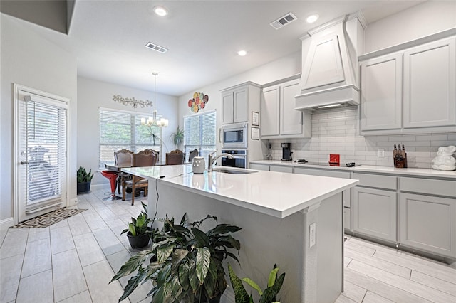 kitchen with appliances with stainless steel finishes, pendant lighting, a kitchen island with sink, and custom range hood