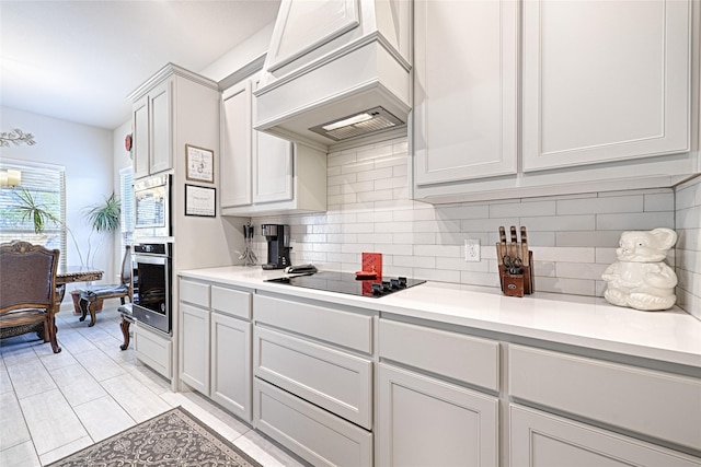 kitchen featuring white cabinets, decorative backsplash, premium range hood, and appliances with stainless steel finishes