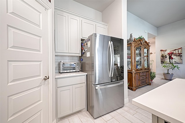 kitchen featuring backsplash, stainless steel refrigerator, and white cabinets