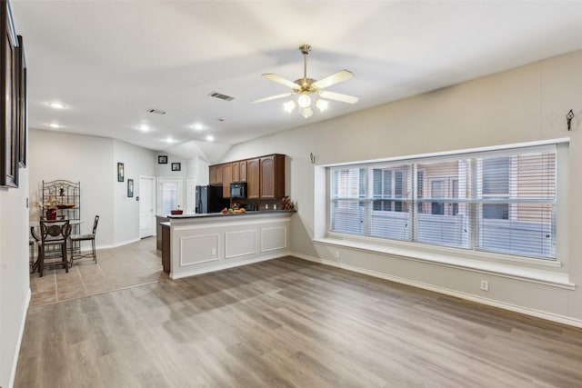 kitchen with kitchen peninsula, light wood-type flooring, vaulted ceiling, ceiling fan, and black appliances