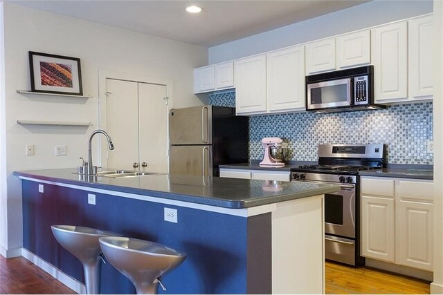 kitchen with decorative backsplash, appliances with stainless steel finishes, light wood-type flooring, sink, and white cabinetry